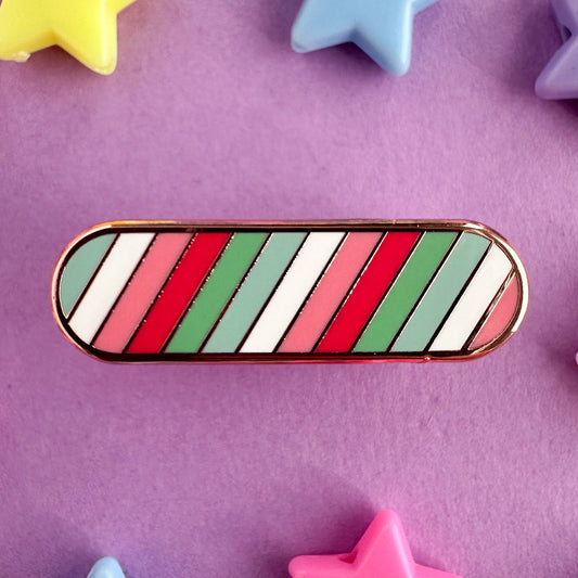 An enamel pin with stripes in the colors of the Abrosexual pride flag in the shape of an oval. The pin is on a purple background with plastic star beads around it