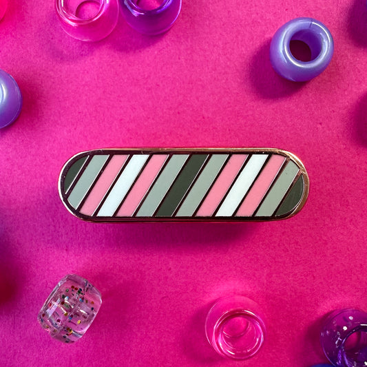 An enamel pin with diagonal stripes in the colors of the Demigirl Pride flag. The pin is on a hot pink background with pony beads around it.