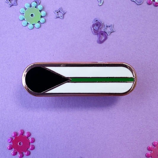 A bandaid shaped pin with the imagery of the Demiromantic pride flag on it, a black triangle an da green stripe on a white background. The pin is on a lavender background with glitter around it. 
