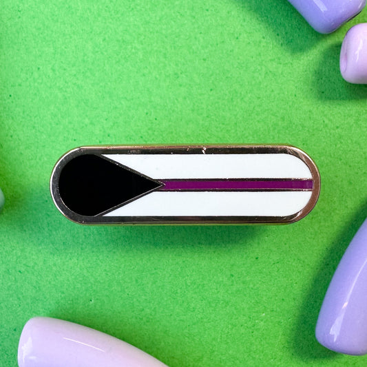 A bandaid with the elements of the Demisexual pride flag on it, a black triangle, purple stripe and white background. The pin is on a green background with pastel beads around it.