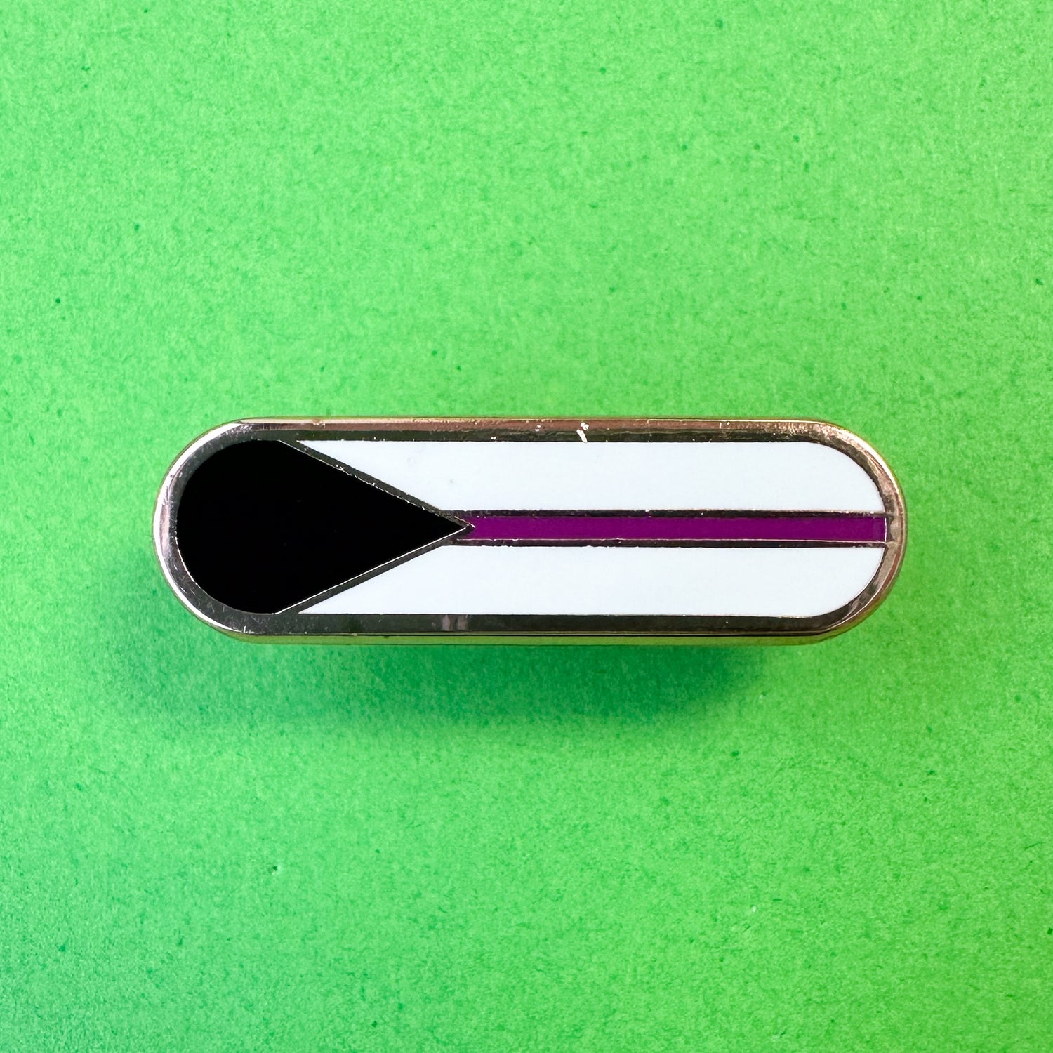A bandaid with the elements of the Demisexual pride flag on it, a black triangle, purple stripe and white background. The pin is on a green background.
