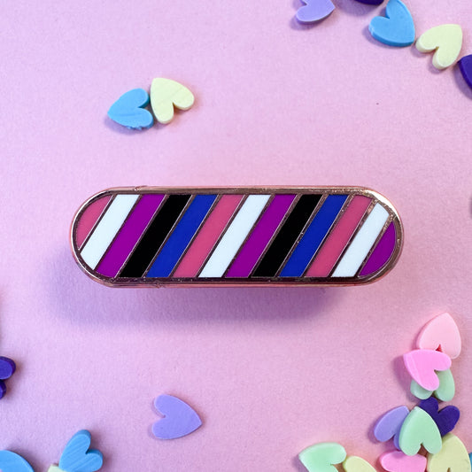 A capsule shaped pin in the colors of the Gender Fluid pride flag on a pink background with pastel heart confetti around it. 