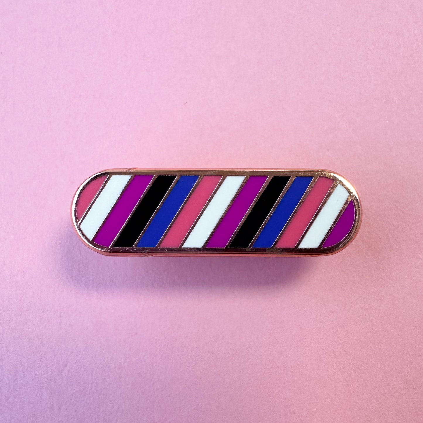 A capsule shaped pin in the colors of the Gender Fluid pride flag on a pink background. 