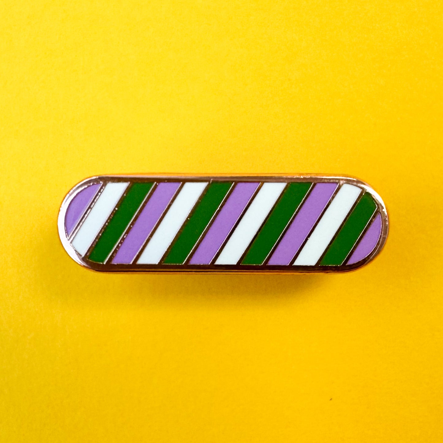 A genderqueer pride enamel pin in the shape of an oval on a yellow background. 