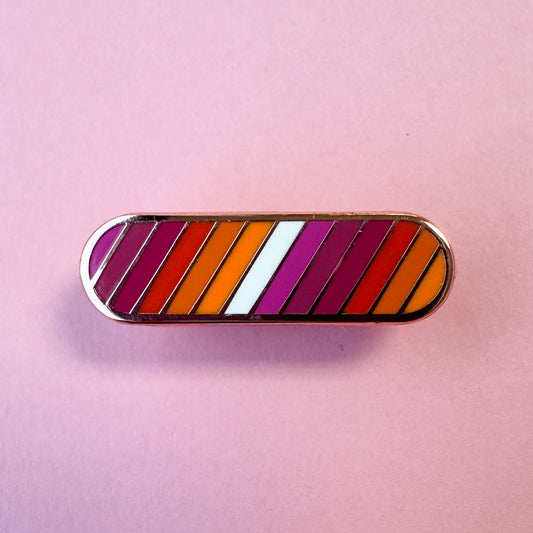 A oval shaped pin with stripes in the colors of the Lesbian Pride flag. The pin is on a pink background.