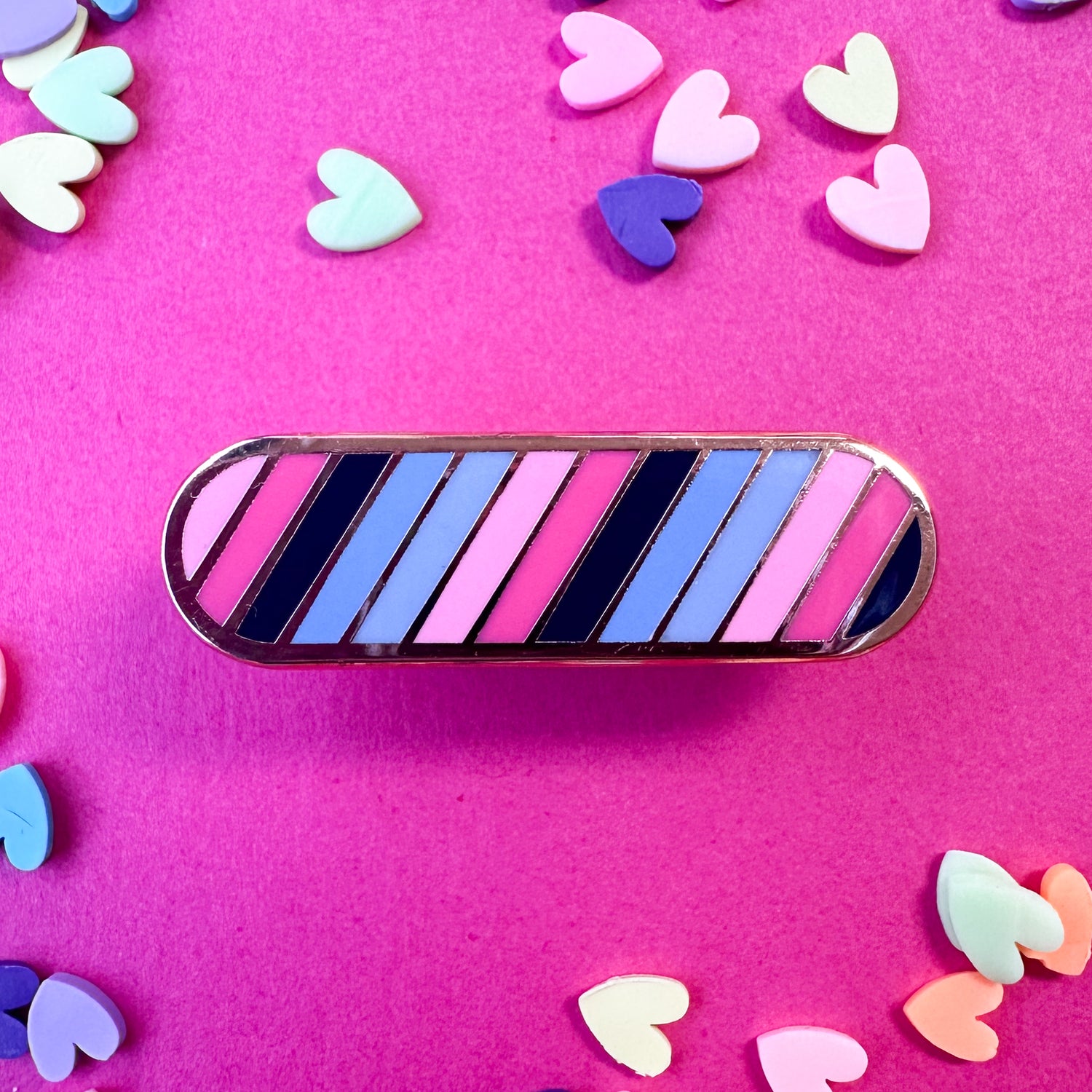 An oval shaped pin with diagonal stripes in the Omnisexual pride flag. The pin is on a hot pink background with heart confetti. 