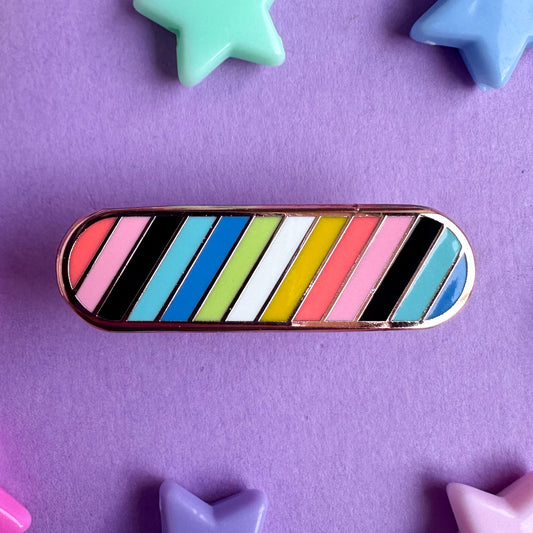 An enamel pin shaped like a bandaid in the colors of the Queer Pride Flag with diagonal stripes. The pin is on a purple background with plastic star beads around it.