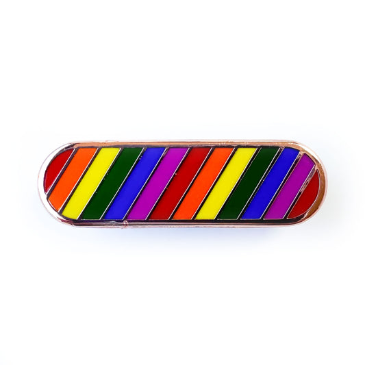 An enamel pin in the shape of a capsule with diagonal rainbow stripes. 
