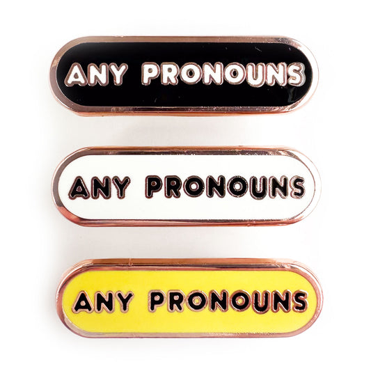 Bandaid shaped pins with the words "any pronouns" on them, the top pin is black, the middle is white and the last one is yellow.