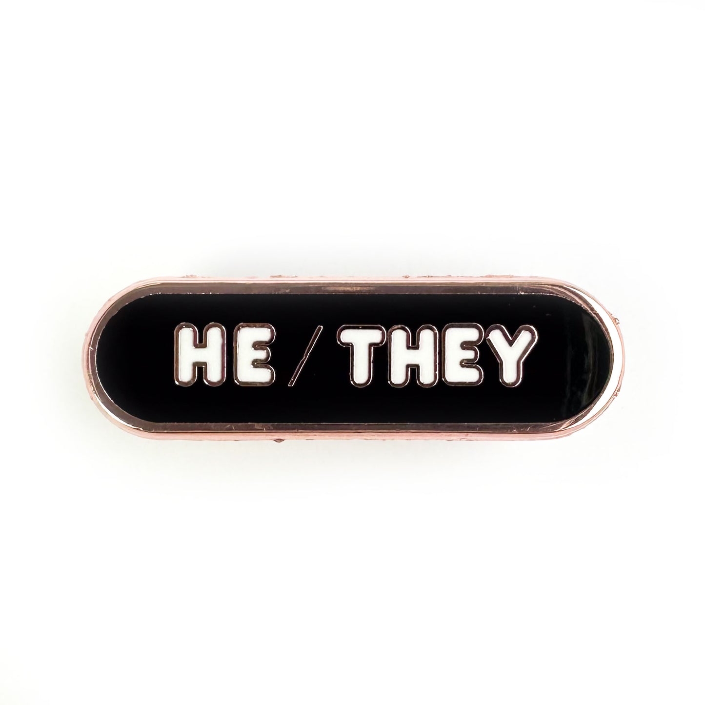 A black oval shaped pin with white words that spell "He/They" to share your pronouns.