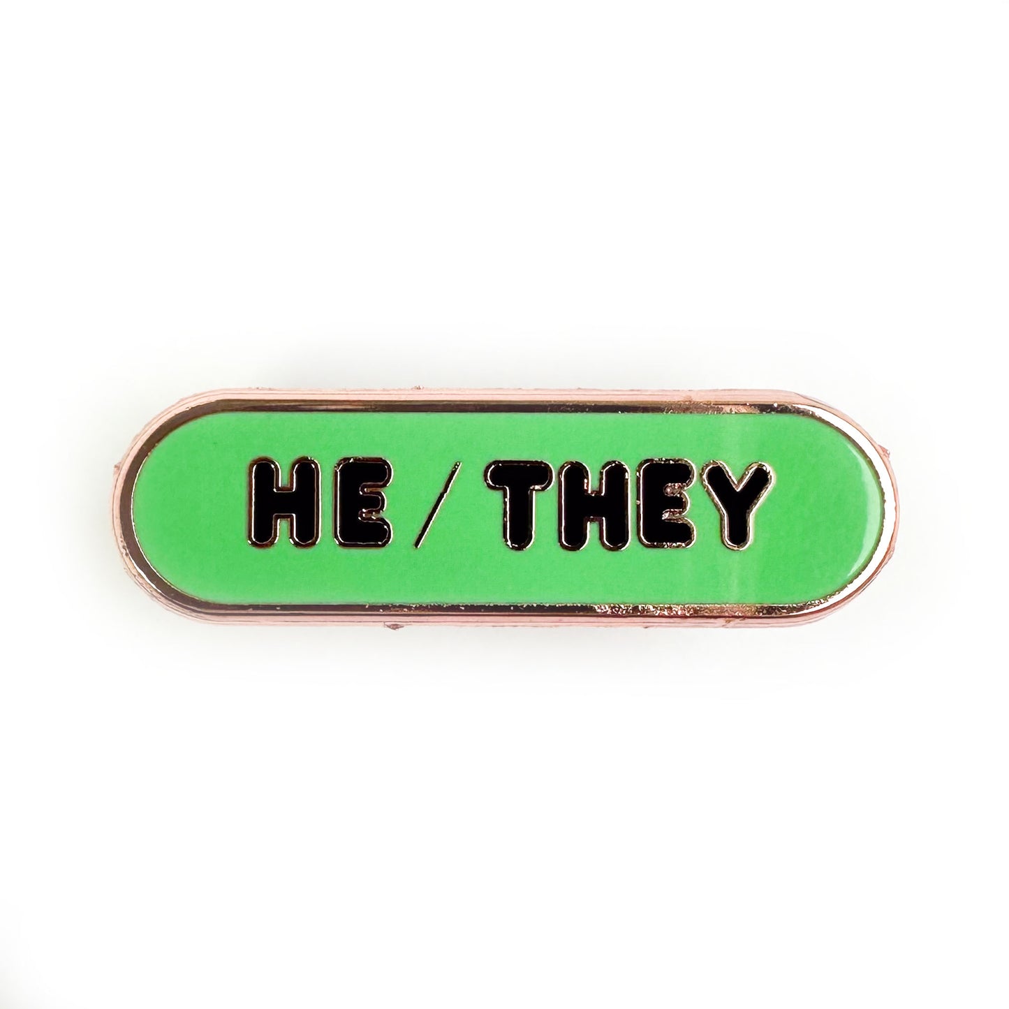 A mint green oval pin with black bubble letters that spell "He/They". 