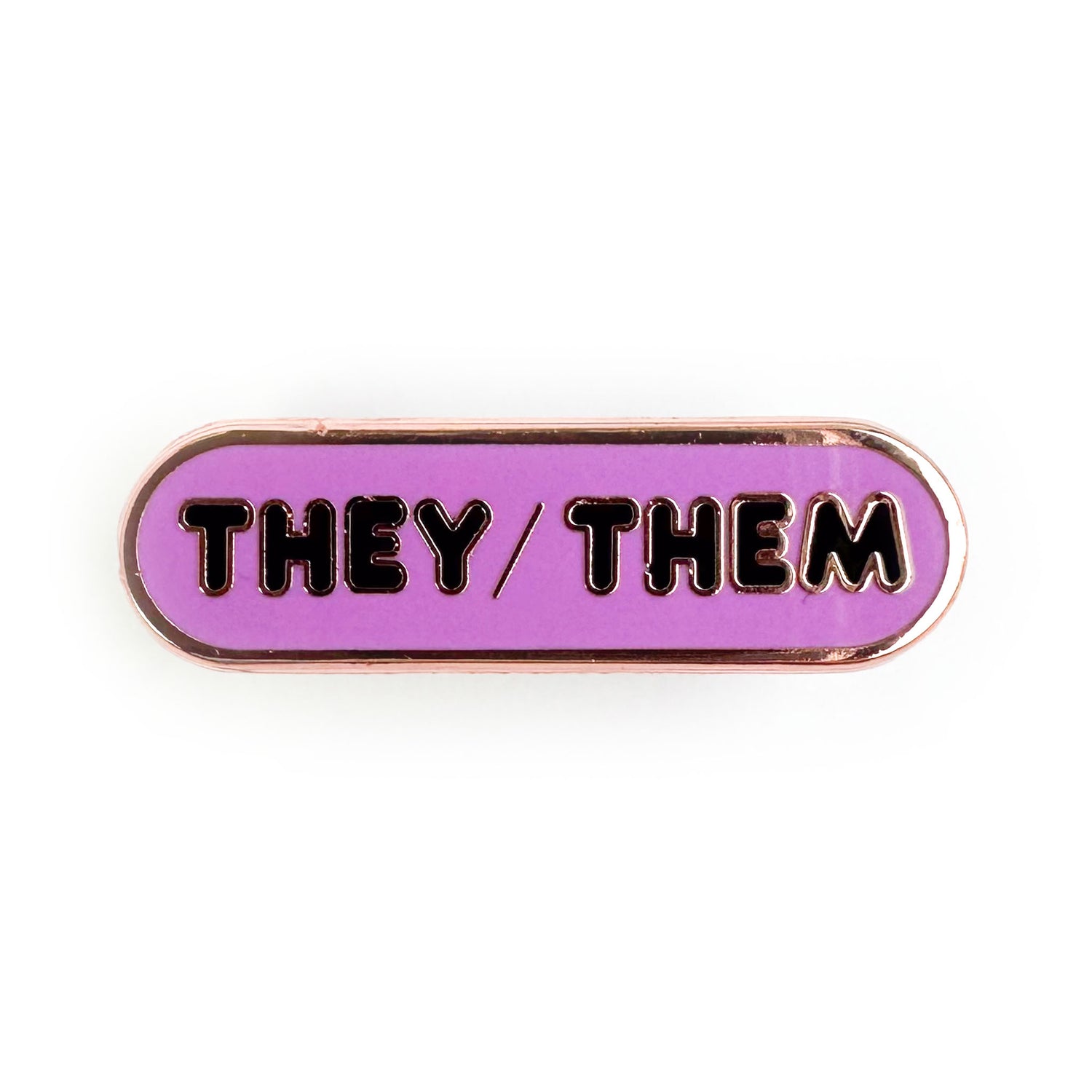 A bandaid shaped pin with a lavender background and black bubble letters on it that spell "They/Them".
