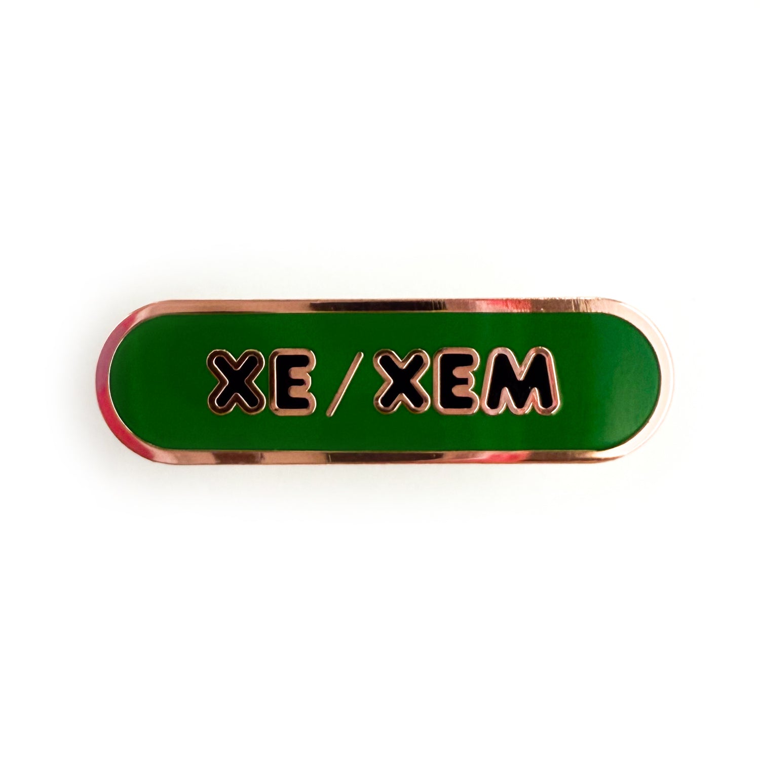 A bandaid shaped pin with the text XE/XEM in bubble letters. The background is green and the text is black.