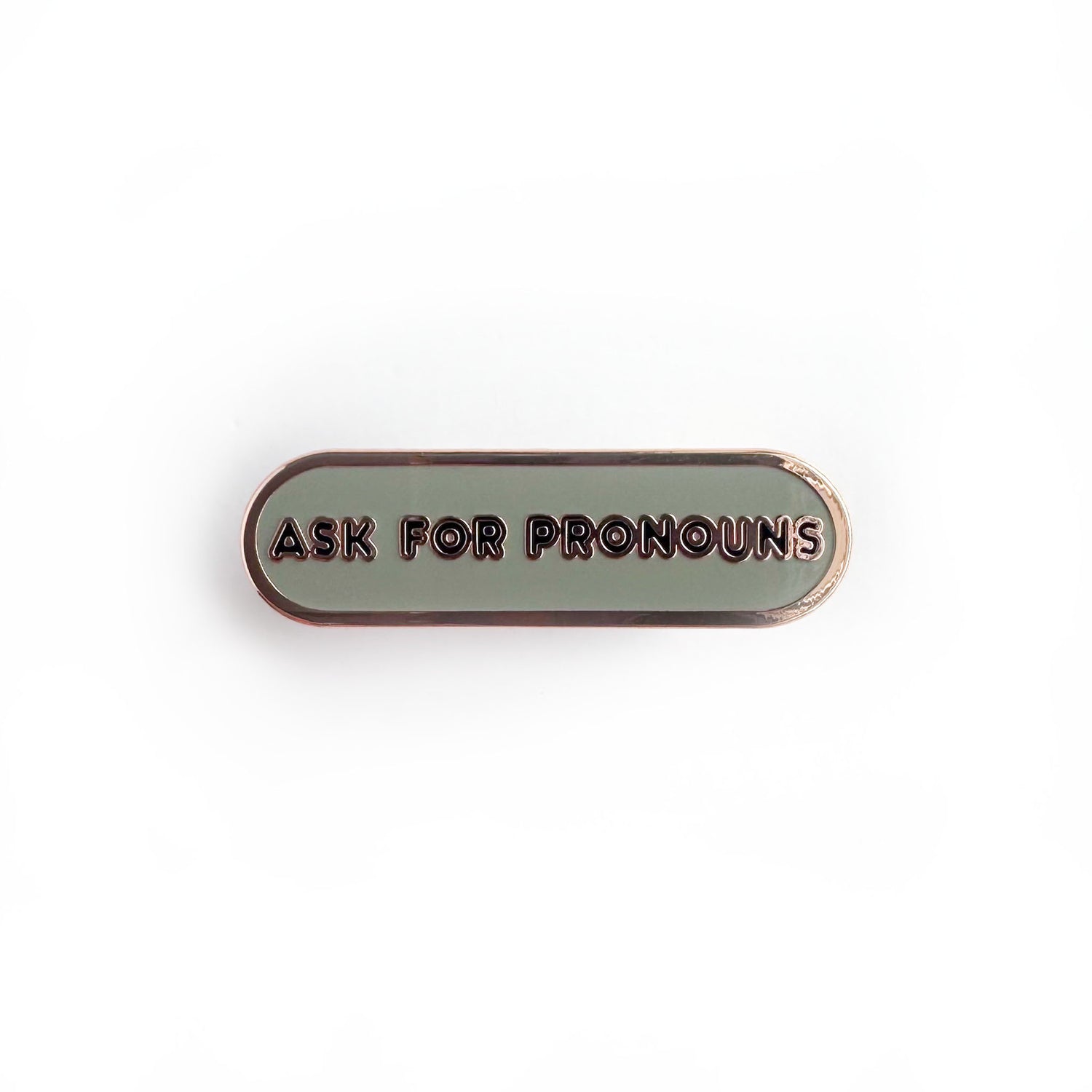 Oval shaped enamel pin with "ask for pronouns" written in black text on a grey background.