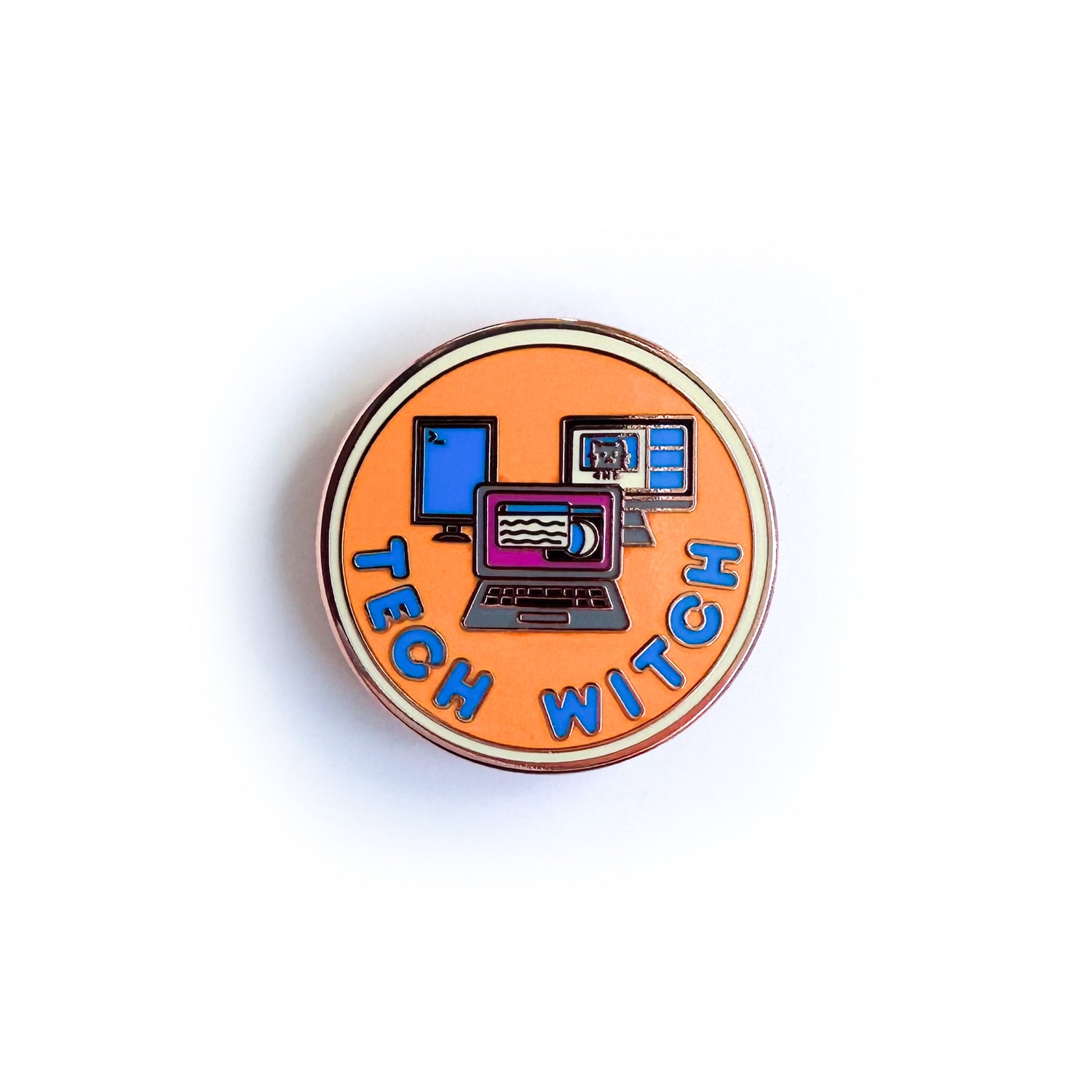 A circular merit badge style pin with the words "Tech Witch" on it. There are images of a laptop surrounded by two computer monitors on it. The pin is orange with a yellow border and blue words. 
