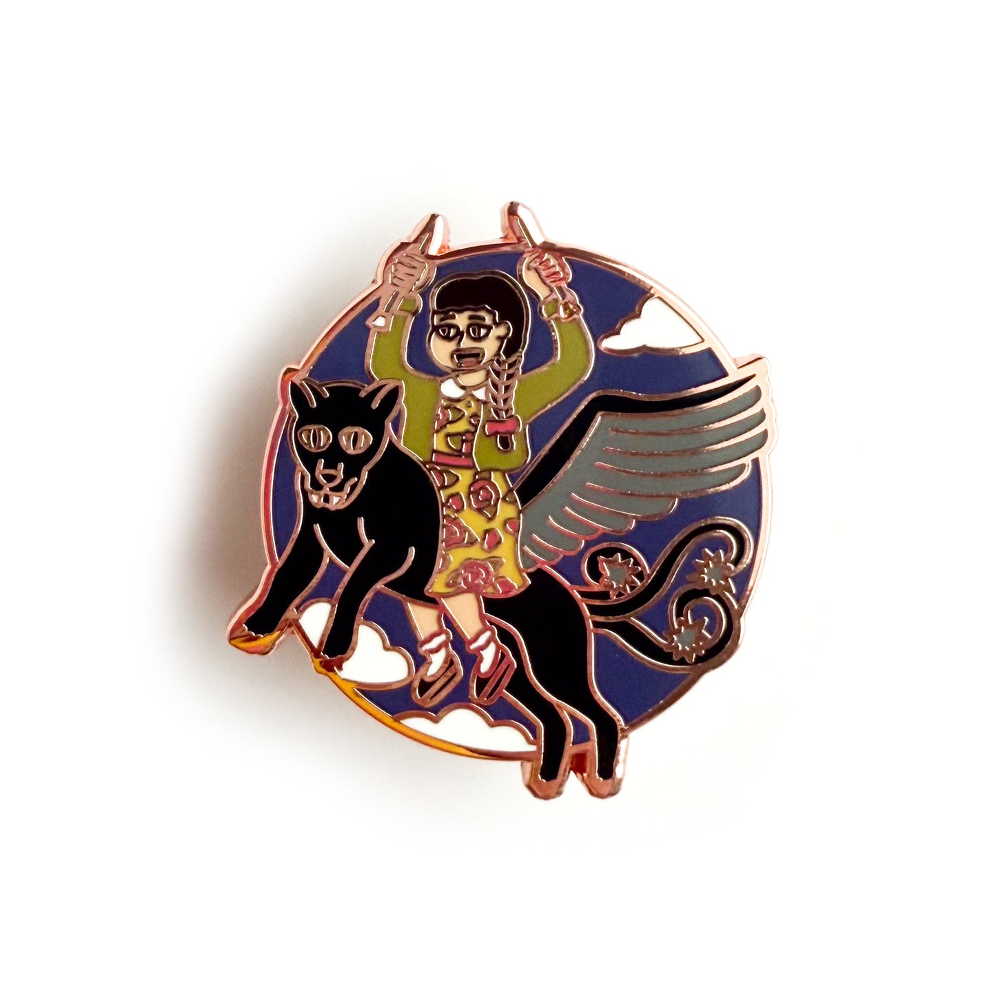 An enamel pin in the shape of a circle with an illustration of a woman holding knitting needles up like daggers wearing a cardigan and a floral dress. The woman is riding a winged jaguar with barbed tails flying through the sky. 