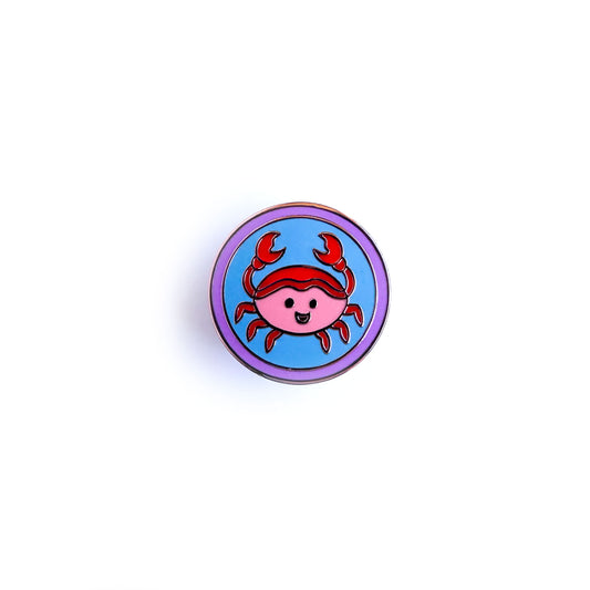 A circular enamel pin with a cute crab design inside to represent the Cancer astrological sign.