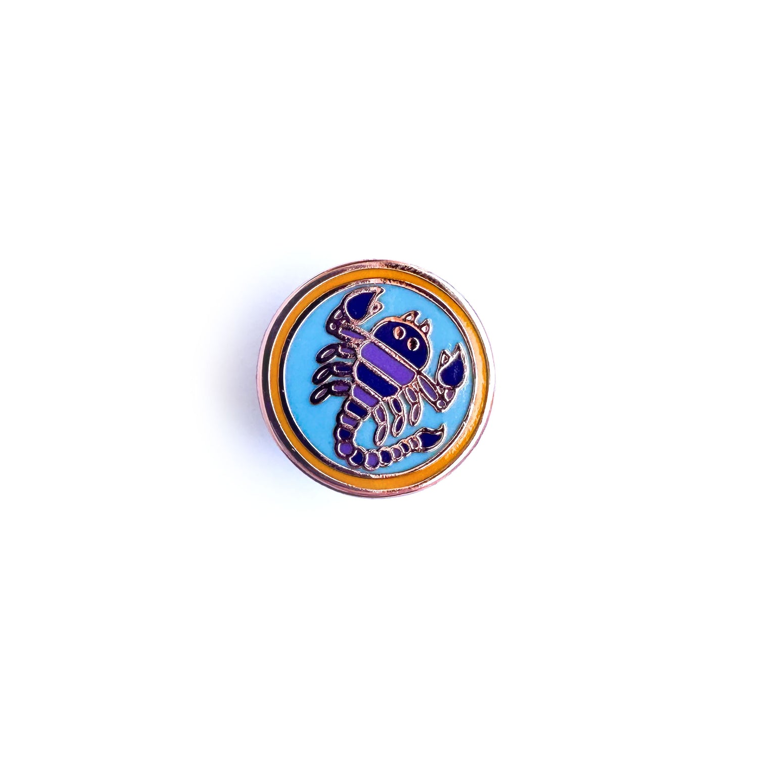 A circle enamel pin with a scorpion in a blue circle inside an orange circle meant to symbolize the Scorpio zodiac sign. 