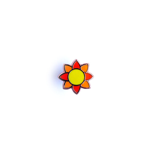 An enamel pin in the shape of an illustration of the sun, with a yellow circle in the middle and orange rays around it.