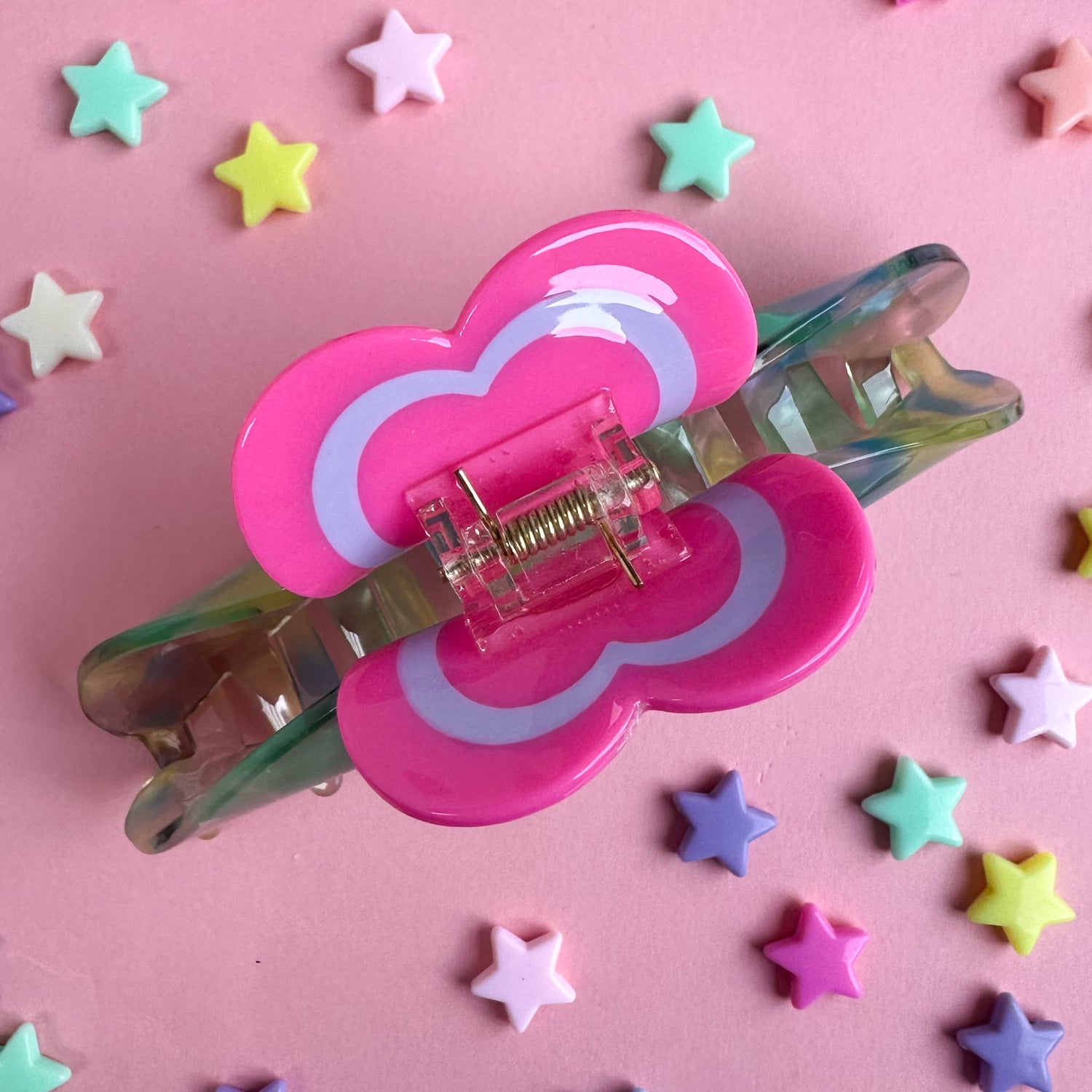 The clip mechanism of a large claw clip with heart handle. The background is pink paper with star beads around it. 