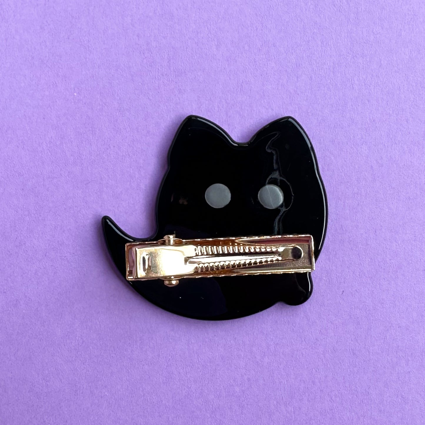 The back of the ghost kitty hair clip which is black with a gold alligator style clip attached. 