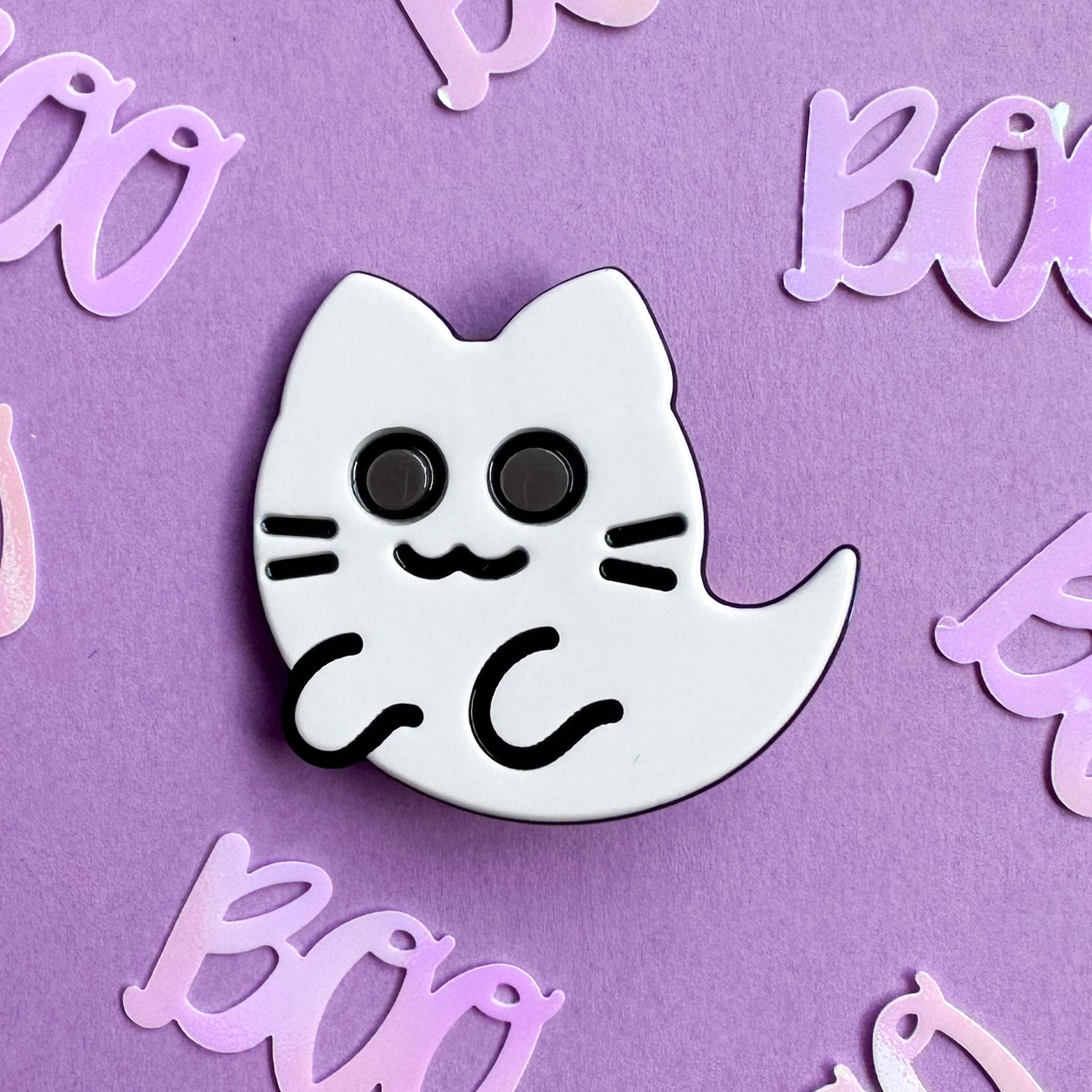 A ghost kitty hair clip made from white and black acetate on a lavender background covered in "Boo" confetti. 