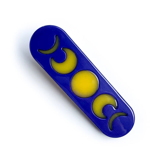 A hair clip shaped like a bandaid that is made from fused acetate with the background as dark purple and the foreground as yellow moon phases.