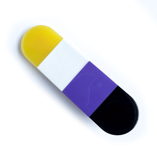 A capsule shaped hair clip with vertical stripes in the colors of the Nonbinary Pride flag, yellow, white, purple and black. 