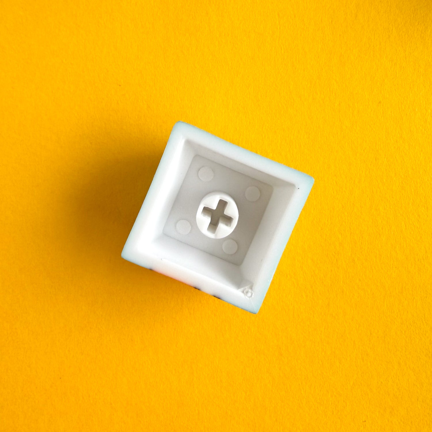 The underside of a keycap for a mechanical keyboard, it is a plastic square with a + shape in the middle of a circle inside. 