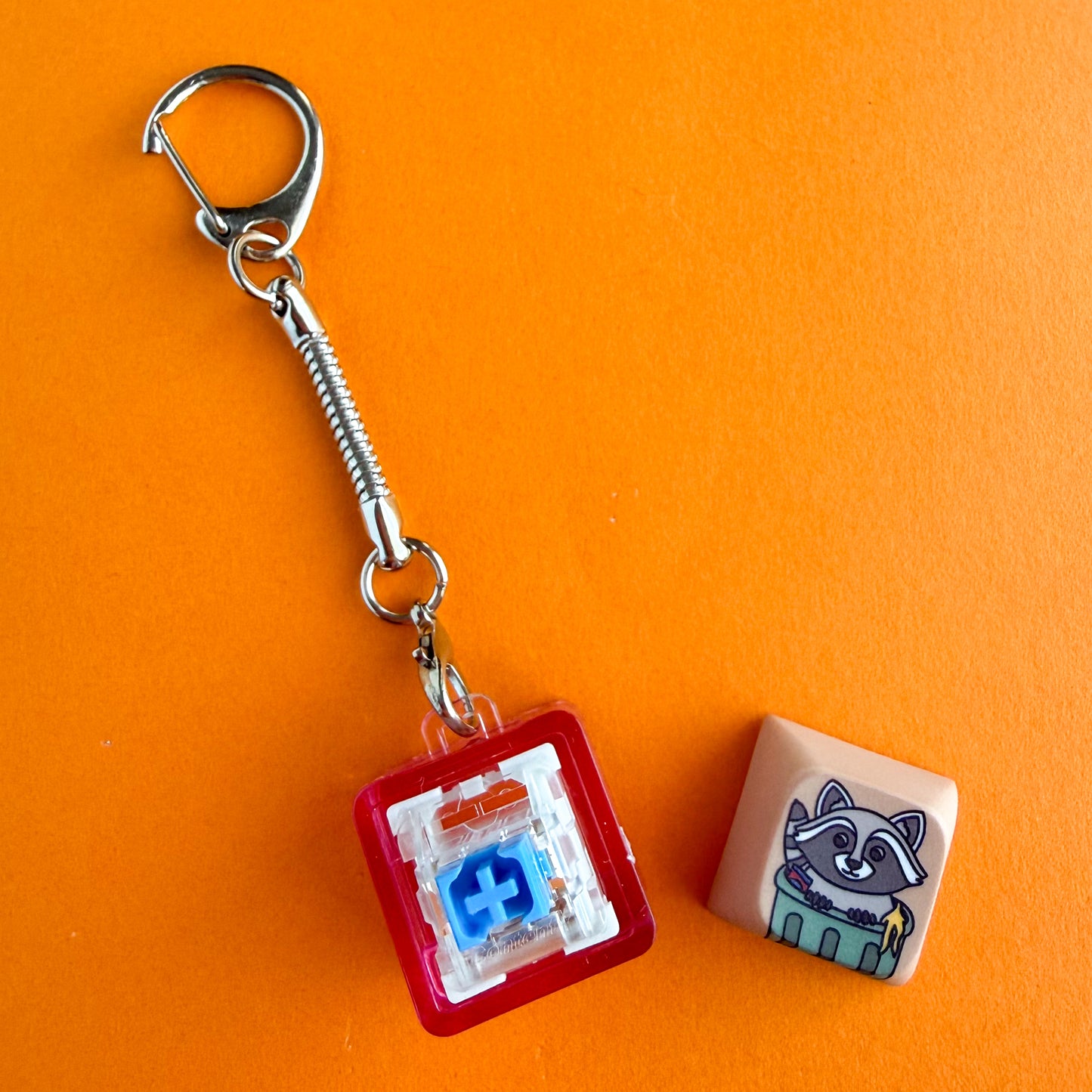 A fidget clicker keychain with the keycap pulled off the top to show the mechanical keyboard switch inside. It is a blue Gateron switch and it is in a hot pink clear keychain housing. 