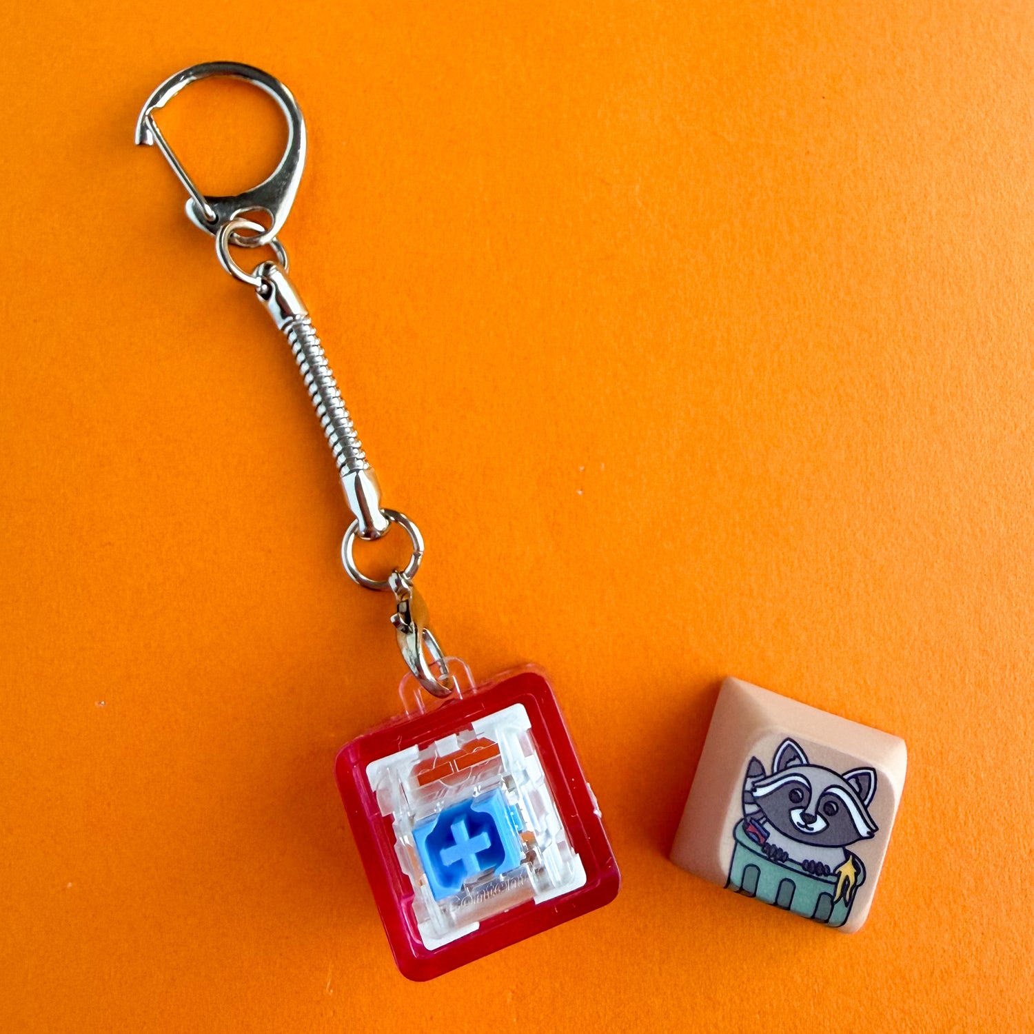 A fidget clicker keychain with the keycap pulled off the top to show the mechanical keyboard switch inside. It is a blue Gateron switch and it is in a hot pink clear keychain housing. 