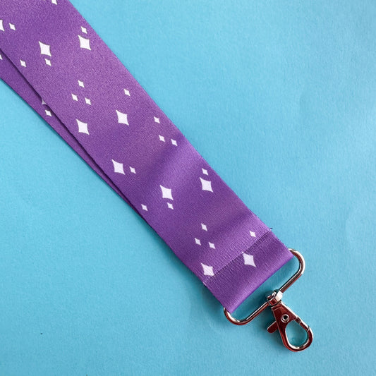 A purple lanyard with white sparkle illustrations on it. The lanyard is on a blue paper background.