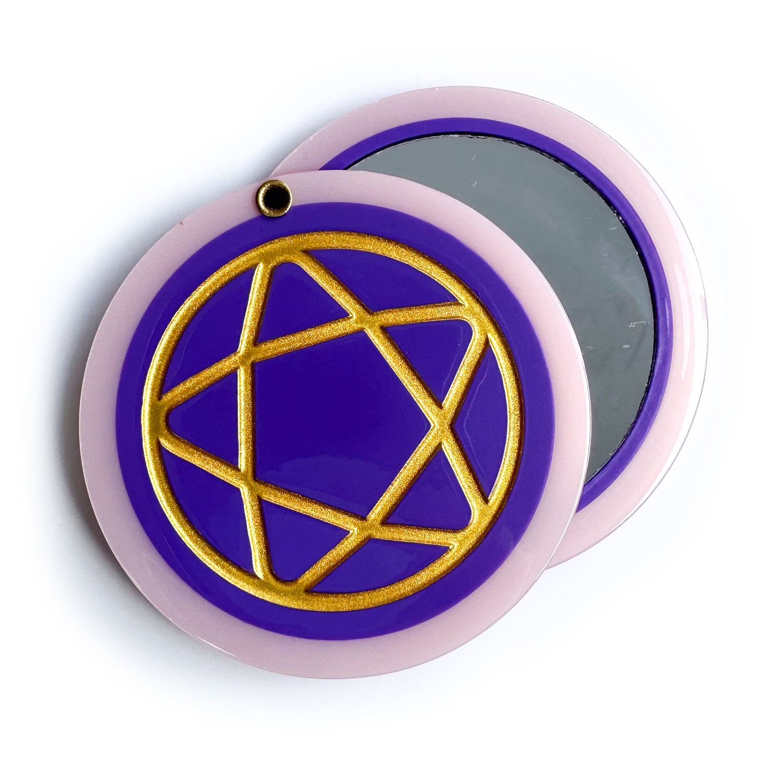 A circular hanged compact mirror that is a purple circle with a pastel pink border with a gold shiny pentacle embossed on the cover. 