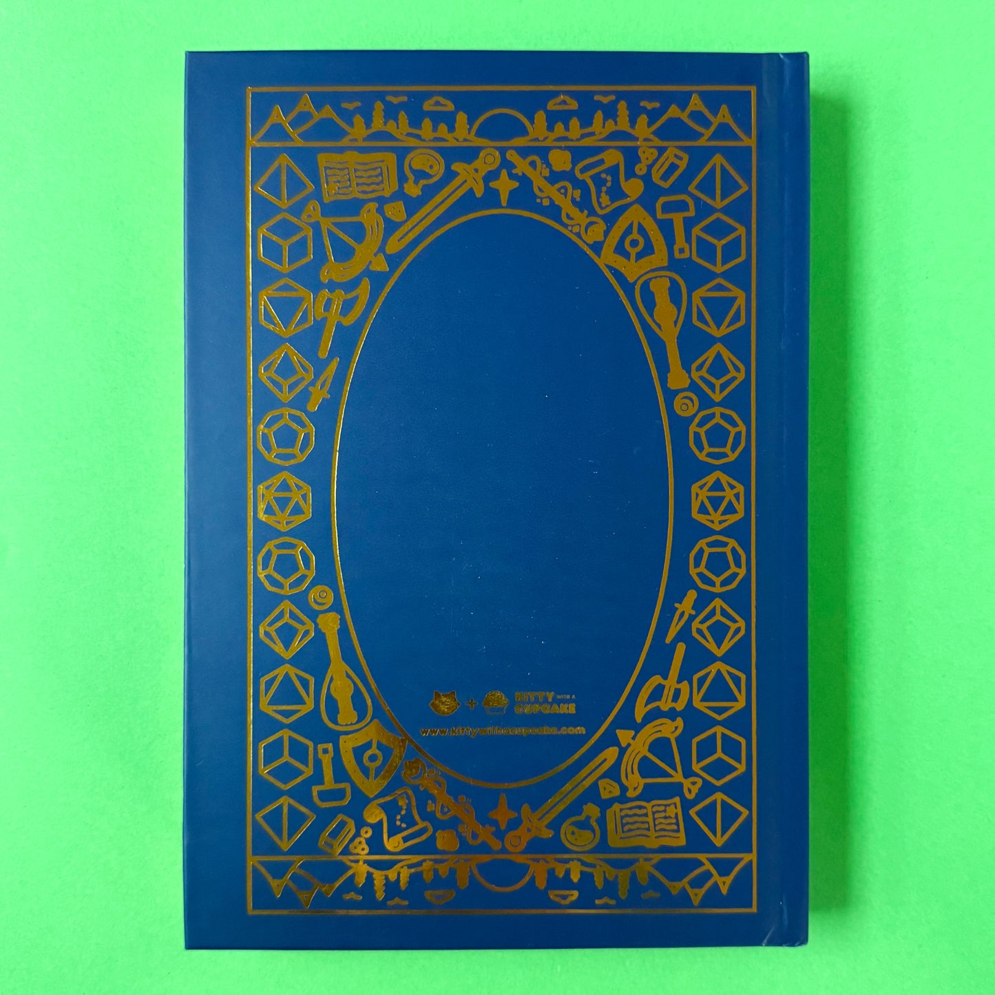 The back of the Adventure Journal on a green background. The back has the same illustrated border as the front, but with the Kitty With a Cupcake logo in the bottom center.