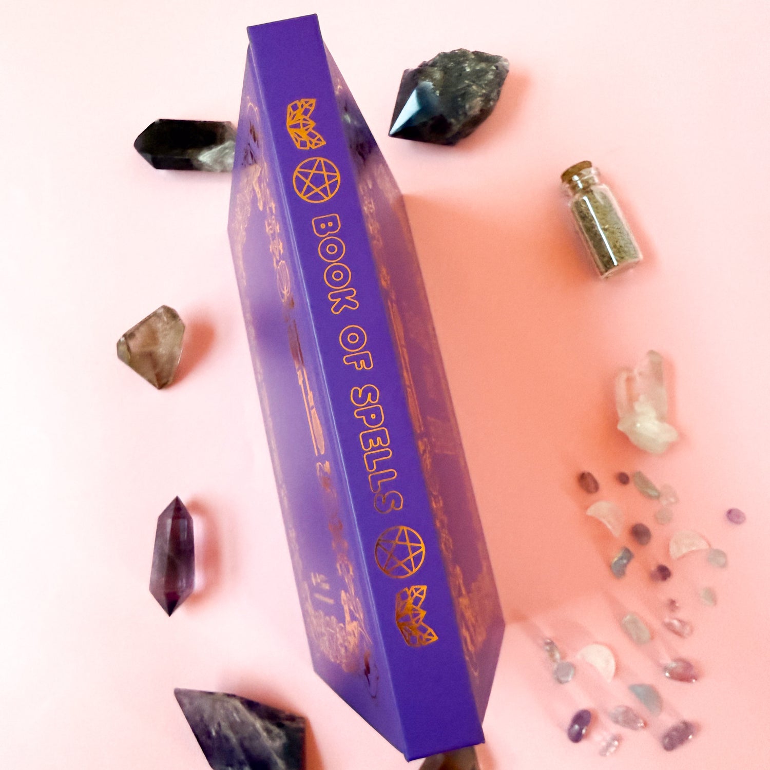 The spine of the Book of Spells displayed surrounded by crystals and spell jars.