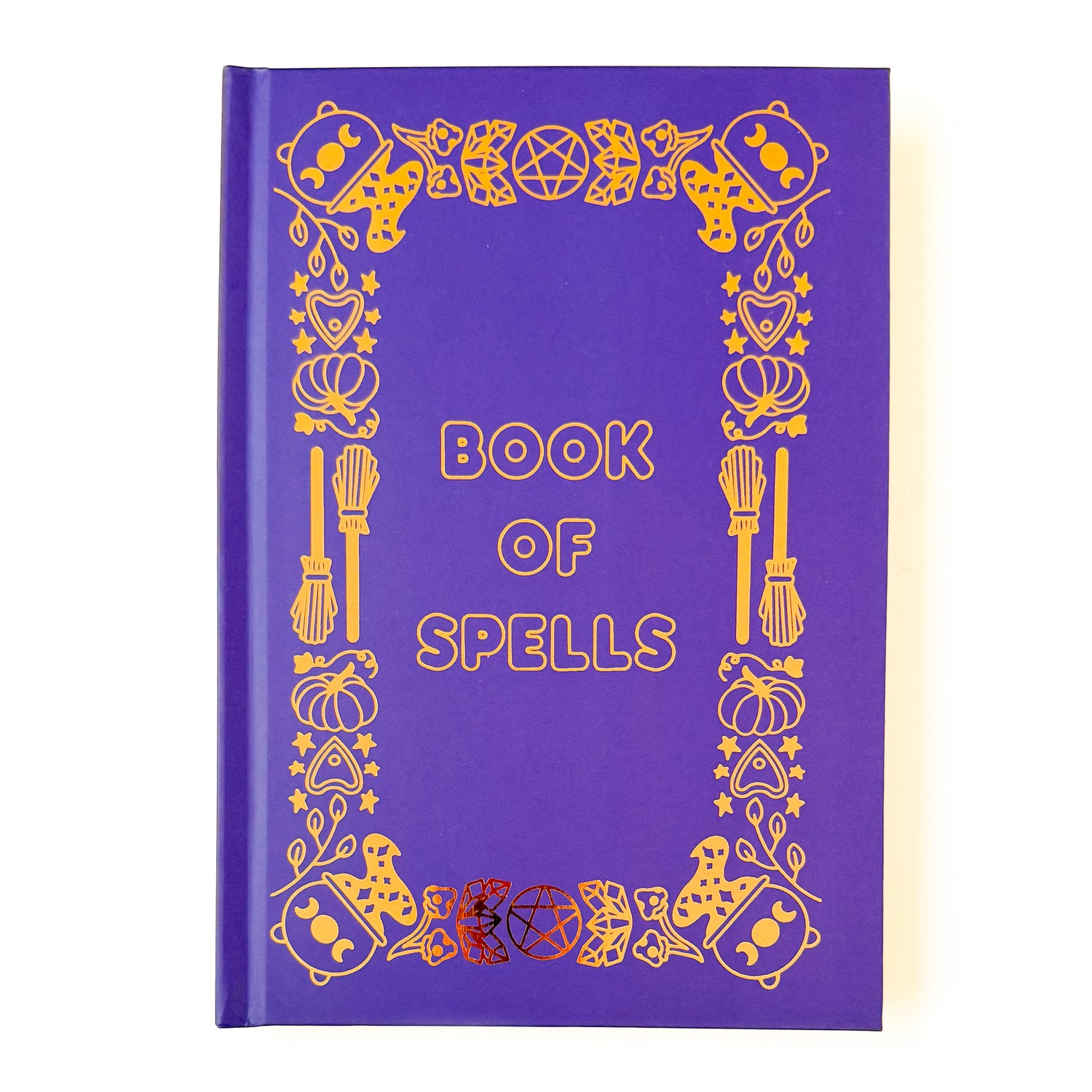 A purple hard covered notebook with gold foil detailing. The title Book of Spells is in the center, and the edges are decorated in witchy illustrations. A few examples of these illustrations are cauldrons, crystals, brooms, and pentacles.   