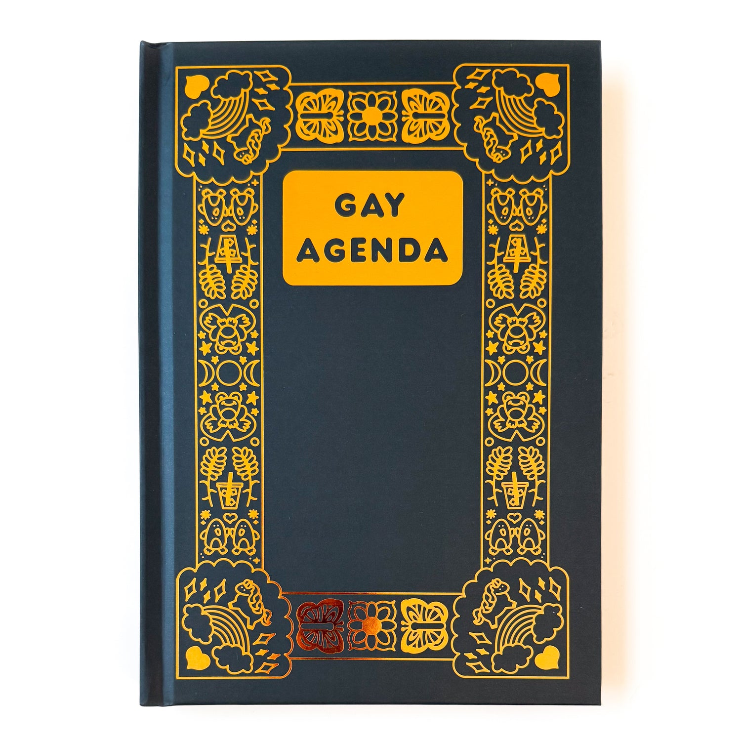 A hard covered black notebook with gold foil details. The title “Gay Agenda” is in the top center, and the notebook has an ornate boarder filled with queer themed illustrations. A few examples of these illustrations are rainbows, unicorns, penguins, butterflies, and iced coffees.