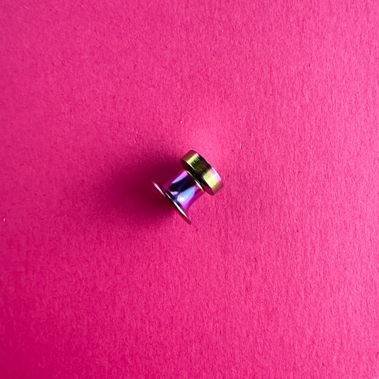 A rainbow magnetic pin back on a pink paper background.