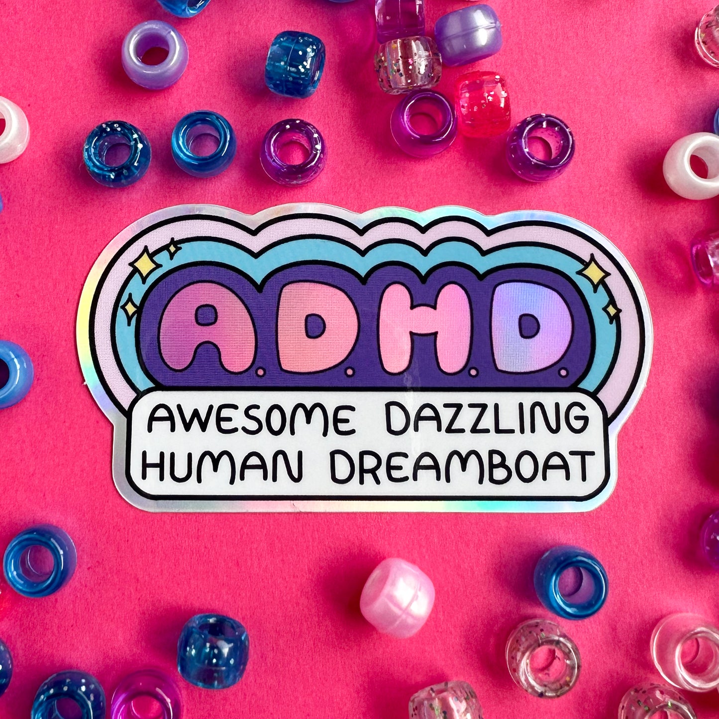 A holographic sticker that reads "A.D.H.D. Awesome Dazzling Human Dreamboat" surrounded by purple, blue, and pink bubble letters on a hot pink background surrounded by glittery pony beads.