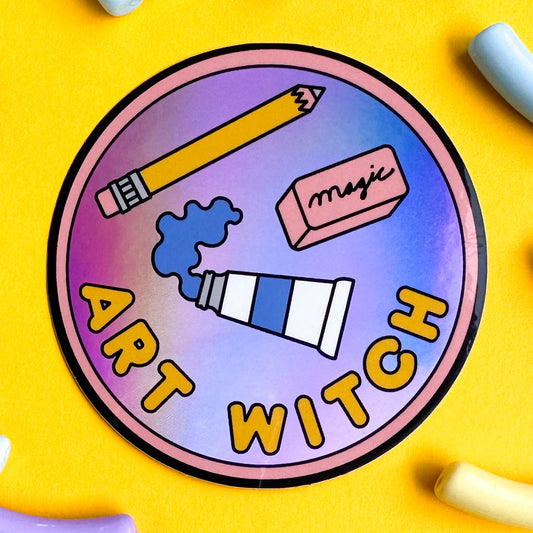 A circular sticker in the style of a merit badge that reads "art witch" it features an illustration of a tube of paint, a yellow pencil, and a pink eraser that reads "magic" on it. 