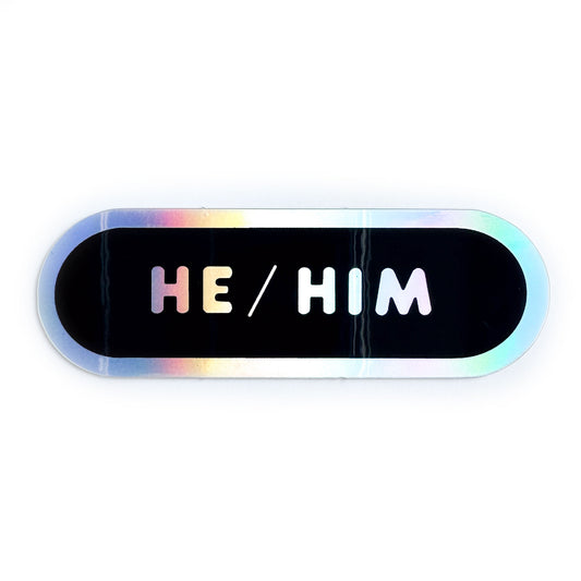 A black capsule sticker with holographic words reading "He/him" on it