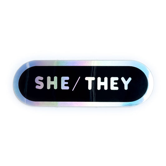 A capsule shaped sticker with the words "She/They" in holographic bubble letters.