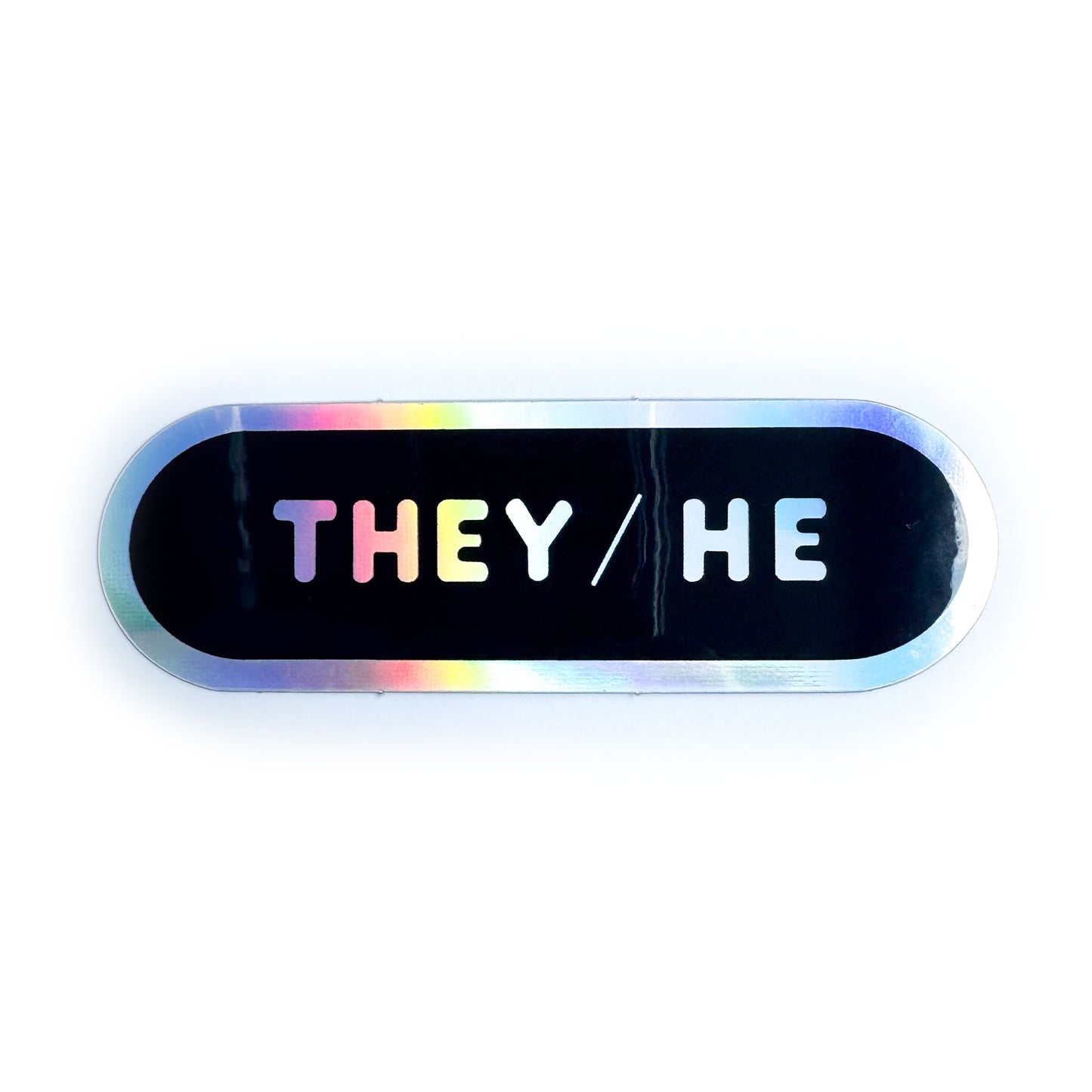 A black capsule shaped sticker with a holographic border and the pronouns They/He in holographic bubble letters.