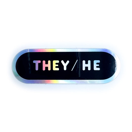 A black capsule shaped sticker with a holographic border and the pronouns They/He in holographic bubble letters.