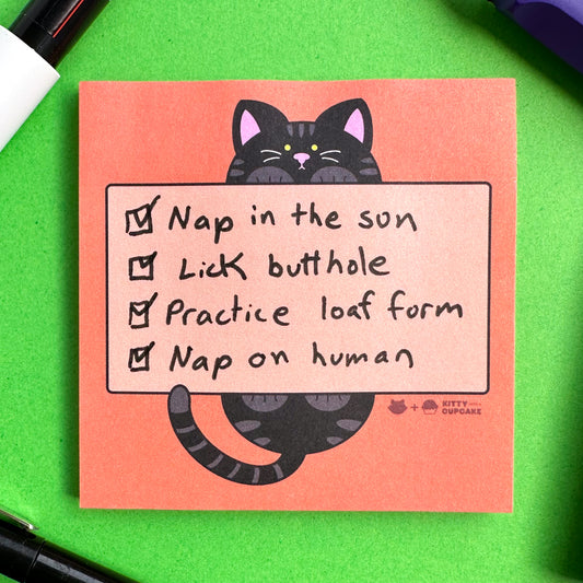 A square orange pad of sticky notes with a black cat holding a light orange box that is an area for writing. There is a to-do list written on the pad that reads, "Nap in the sun, Lick butthole, Practice loaf form, Nap on human" all of the items on the list are checked off. 