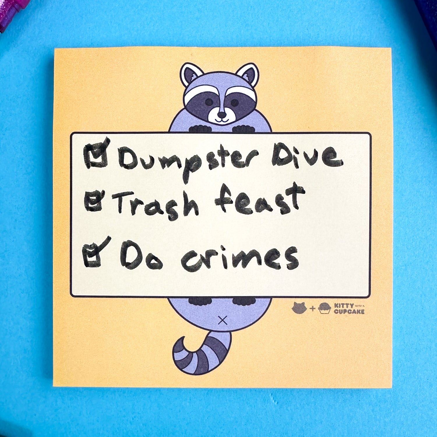 Square yellow sticky notes with a raccoon illustration holding a light yellow box that has a checklist that reads " Dumpster Dive, Trash feast, Do crimes" hand written in it. 