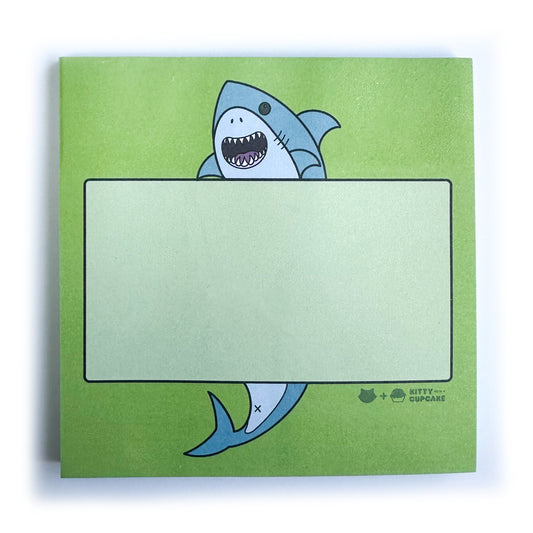 A lime green pad of sticky notes with an illustration of a shark holding a lighter green box to write in.