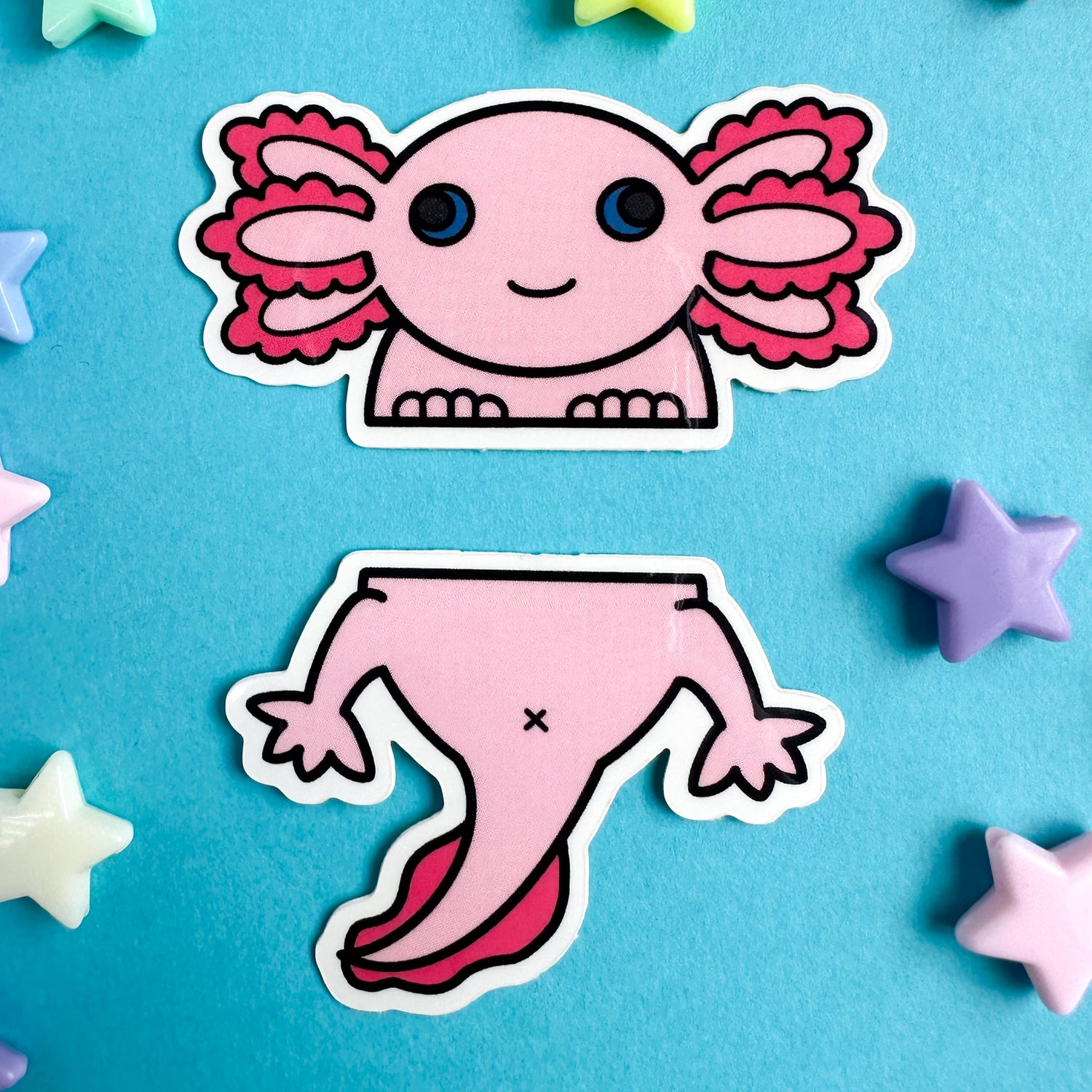 A cute Axolotl sticker set, one is the top half and one is the bottom. The stickers are on a blue paper background with star beads around them. 