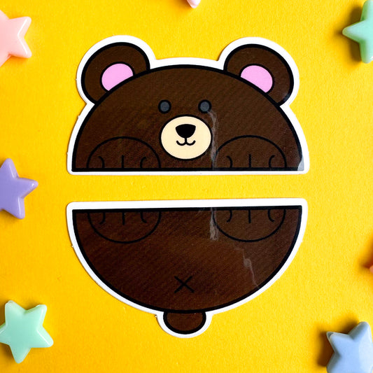 Two vinyl stickers that come together to form a bear that is cut in half horizontally. The top sticker is the bears's head and front paws and the bottom is the bear's tail bottom paws. The stickers are on a yellow paper background