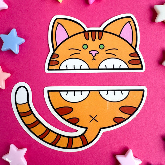 Two vinyl stickers form an orange cat cut in half horizontally across the middle. The top half is the head and front paws, the bottom half is the back paws and tail. The stickers are sitting on a pink background with plastic star beads around them.